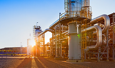 The sun is setting behind a large industrial plant